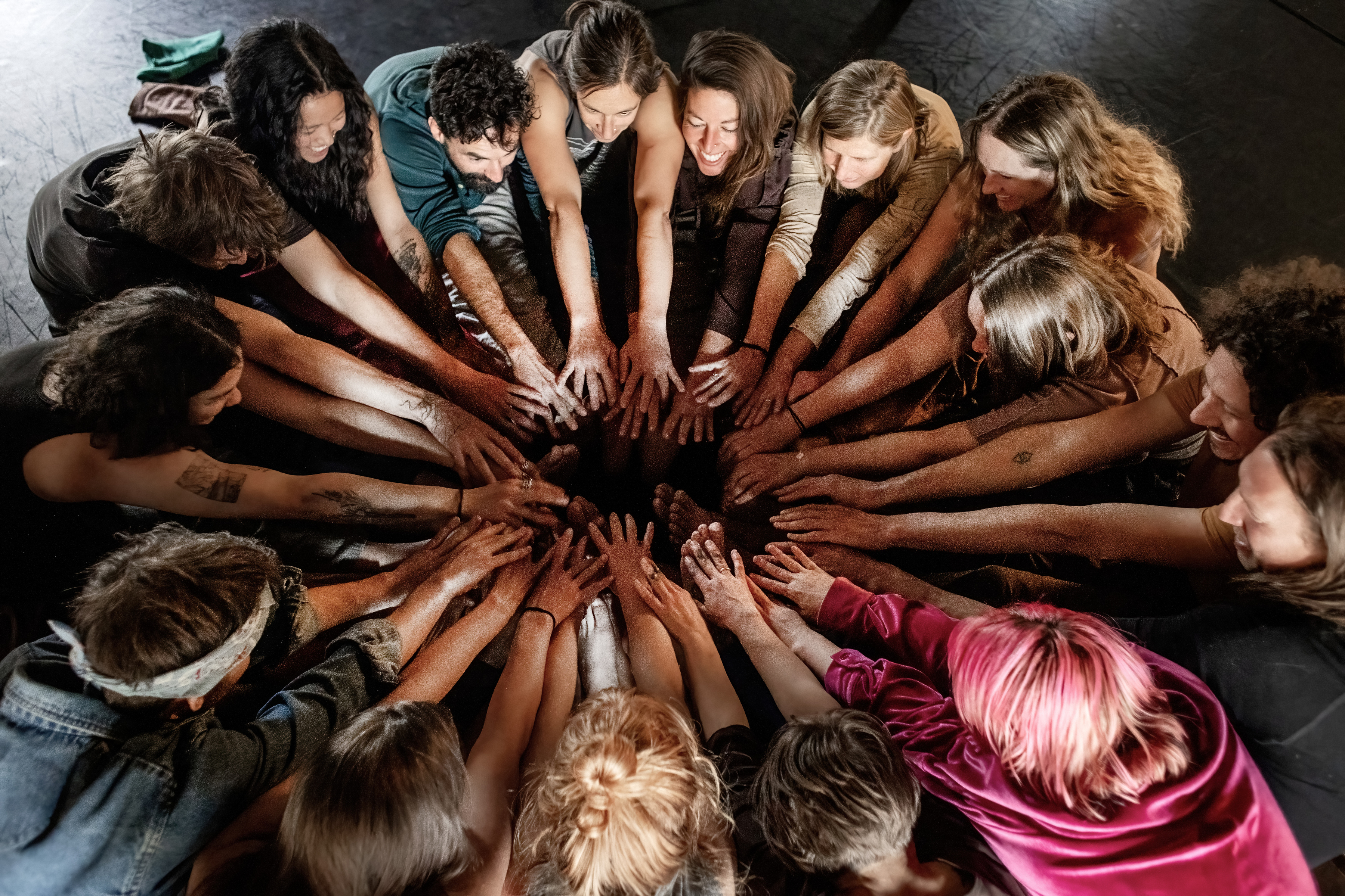 A large circle of Contact Improvisation dancers with hands joined in the center